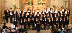 Der Kinder- und Jugendchor der Singschule an St. Petri steht vor dem Altar der Kirche und wird von Bernadette dirigiert