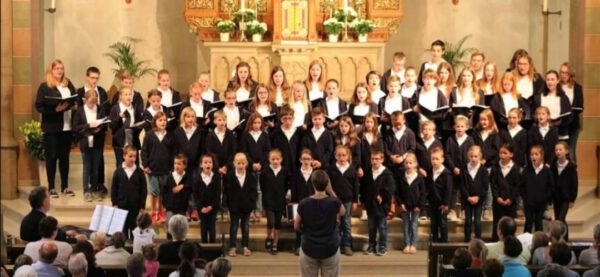 Kinder und Jugendliche vor einem Altar in Chorformation stehend, Bernadette als Dirigentin davor