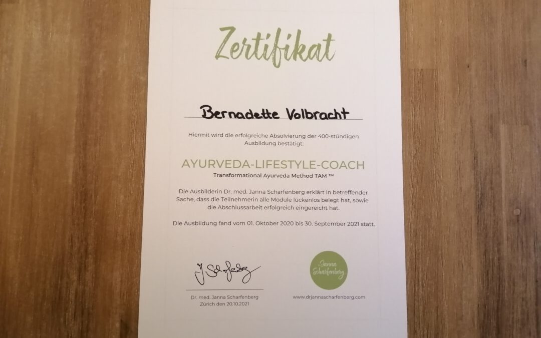 Bernadettes Zertifikat zum Ayurveda-Lifestyle-Coach liegt auf einem Holztisch.