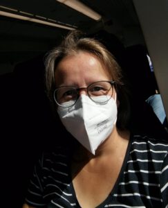 Bernadette trägt eine FFP2-Maske und sitzt im Zug