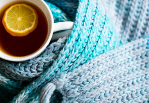 Ein blauer Schal auf dem eine Tasse mit Tee steht - Wärme hilft Dir bei einer Erkältung!
